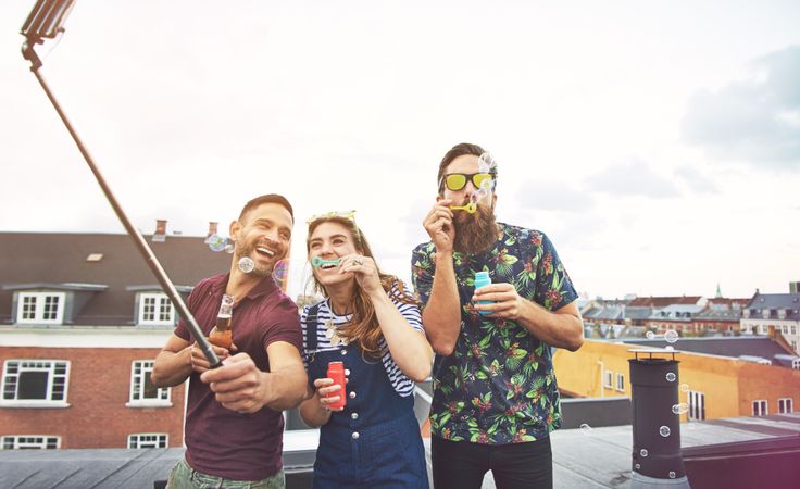 Group of friends blowing bubbles on roof with selfie stick