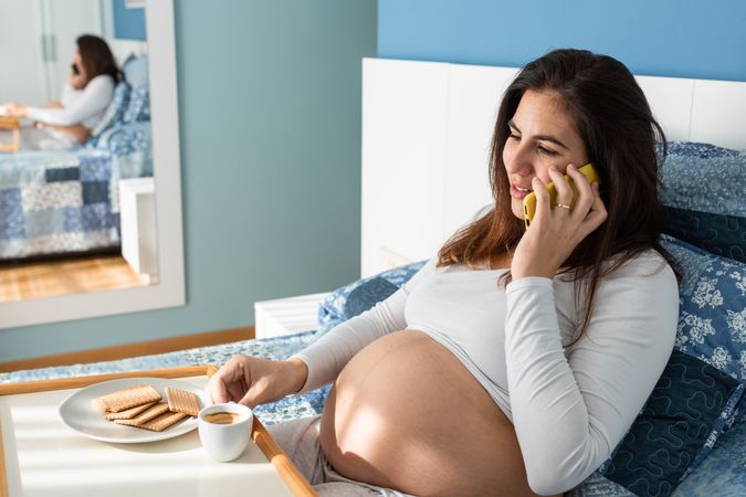 Cheerful pregnant woman speaking on smartphone during breakfast