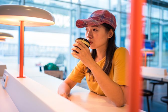 Asian woman drinking coffee at table under lighting lamp