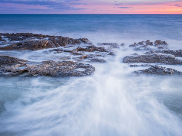 Sea waving near rough rocks during sunset