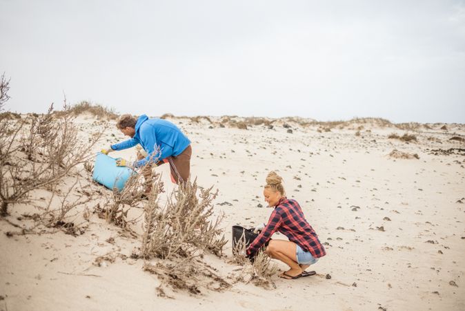 Content modern woman and man picking litter from sandy seashore