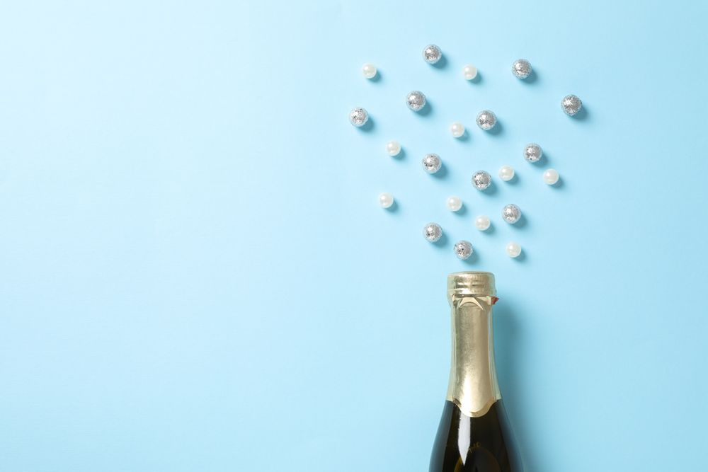 Champagne bottle and glitter on blue background, space for text