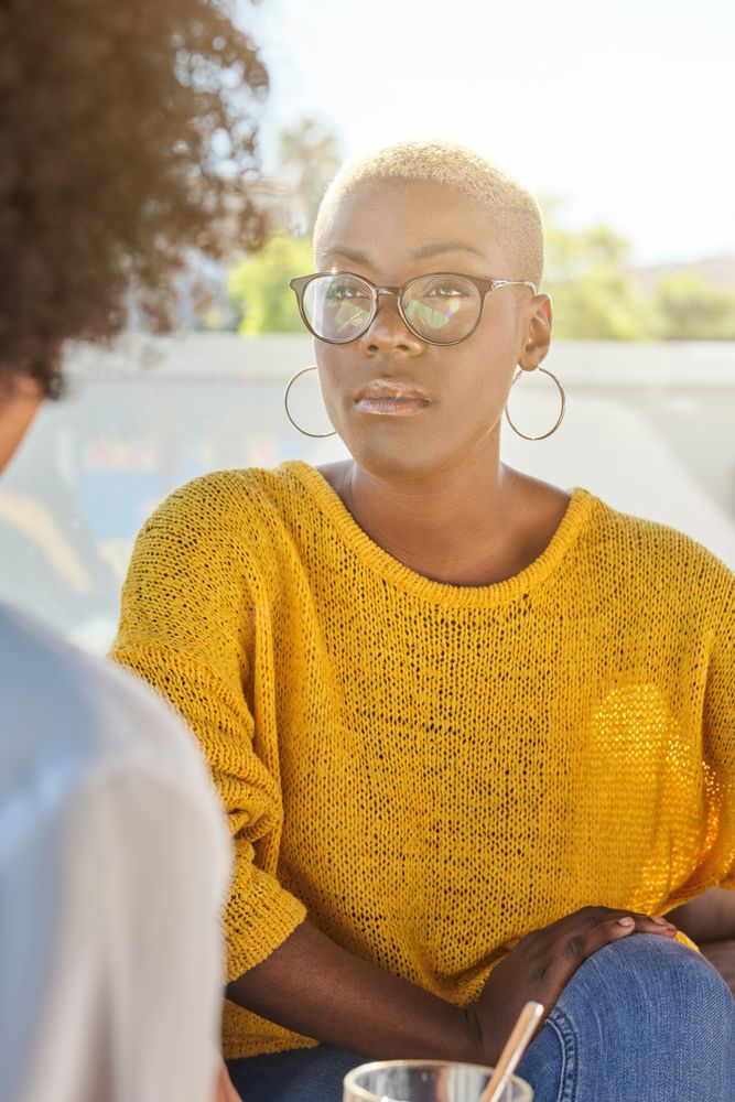 Thoughtful Black woman in yellow sweater listening to friend