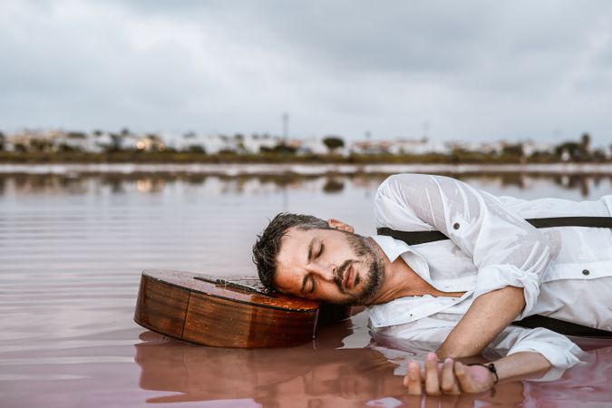Man resting in water with guitar at seaside