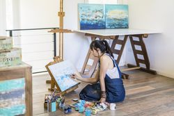 Woman artist painting on a canvas a blue abstract painting. Creative ywoman working on the floor in her art studio.