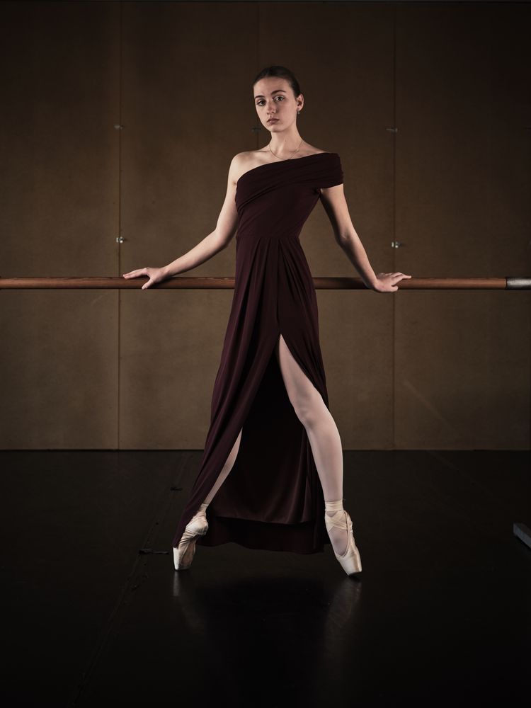 Stylish ballerina in pointe shoes leaning on barre