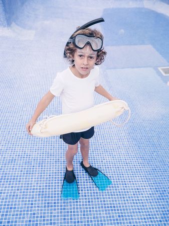 Confused boy with swimming ring and mask in empty pool