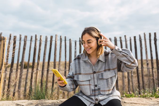 Happy young woman using smartphone and listening to music in headphones in countryside