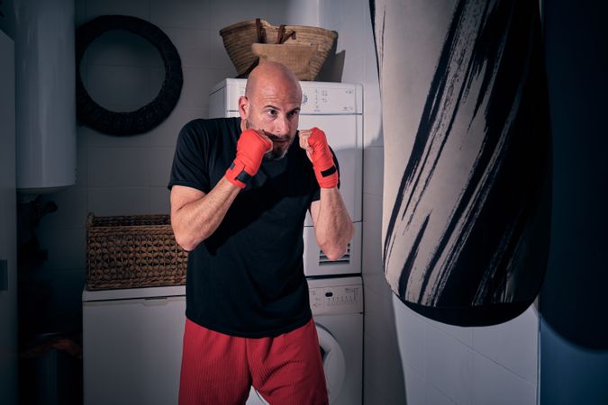 Man training boxing in the laundry room at home with a bag