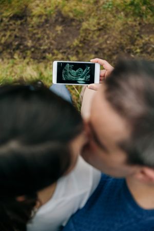 Pregnant couple looking ultrasound on the mobile with her husband and kissing