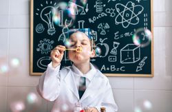 Kid doing soap bubbles against drawings on chalkboard