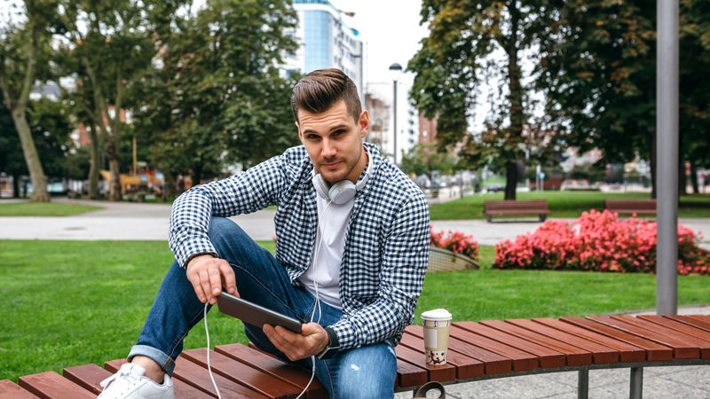Young man looking camera using tablet outdoors