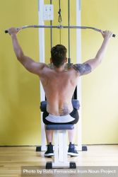 Back of tattooed male exercising his arms on weight machine 0VZ2O0