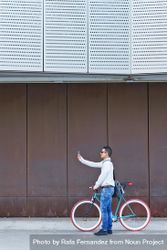 Male in sunglasses standing with red and green bicycle taking photo parked against a brown wall 5RQxJ0