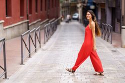 A woman dressed in a striking red jumpsuit is confidently walking down an urban street