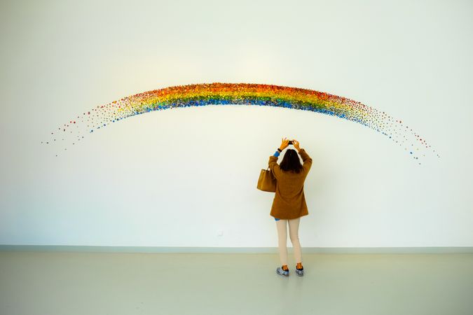 Back view of woman taking photo of the rainbow painted with one brush on the wall