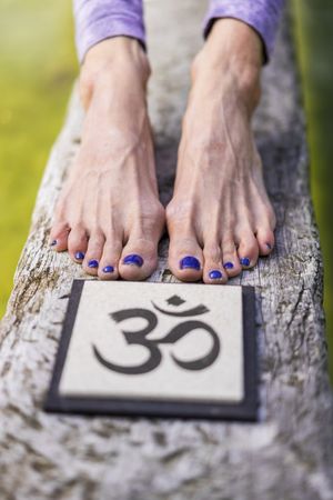 Close up of woman's feet behind an Om sign on a tree trunk over the water.