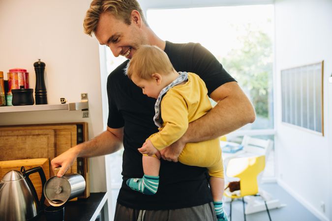 Father carrying his baby and preparing coffee in kitchen