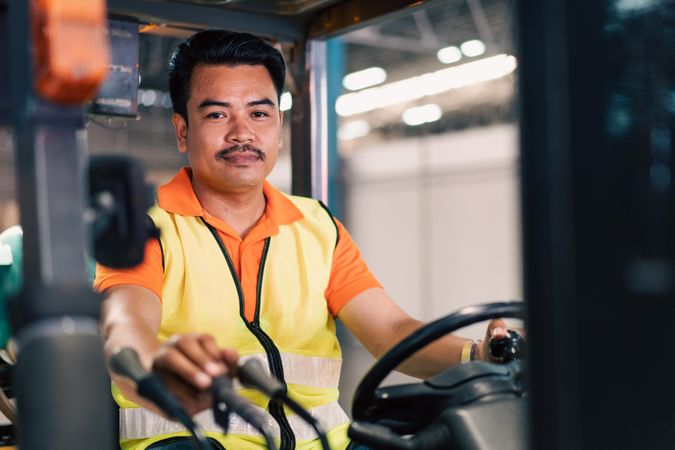 Man in high visibility vest driving forklift in factory