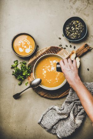 Pumpkin soup with garnishes on concrete, with hand pouring cream