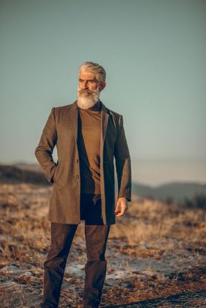 Man in brown coat standing on brown grass field during golden hours