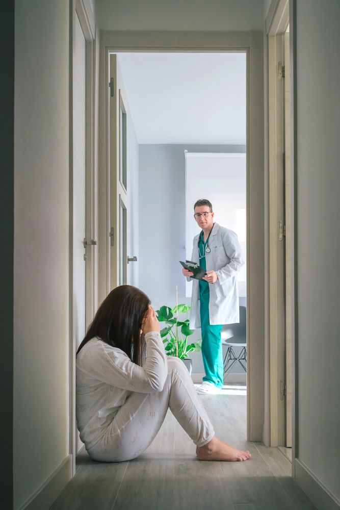 Physician looking at female patient sitting on floor in mental health center