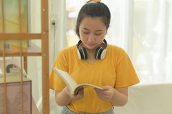 Asian woman standing reading a book with smiling face.