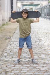 A teenage boy carrying skateboard behind head and smiling
