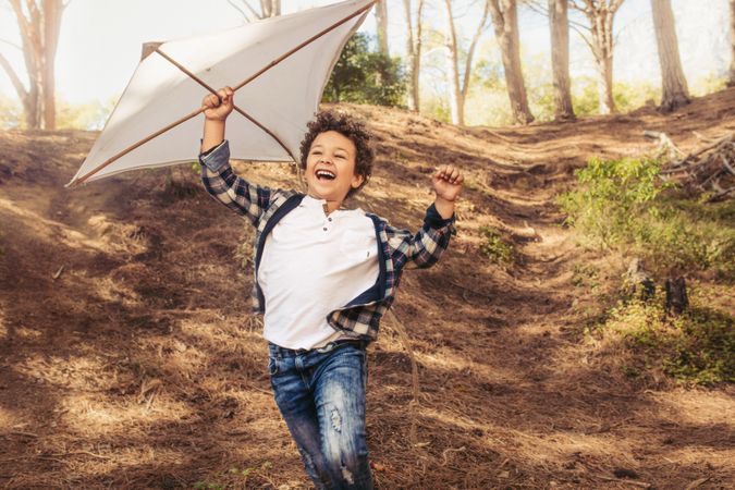 Cheerful boy running downhill with a kite in hand