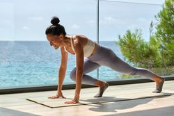 Slim sportswoman training on terrace against ocean in sunlight