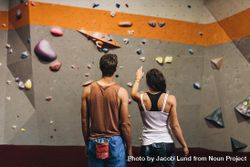 Rear view of female instructor giving instructions to man on rock climbing wall bEzWn0