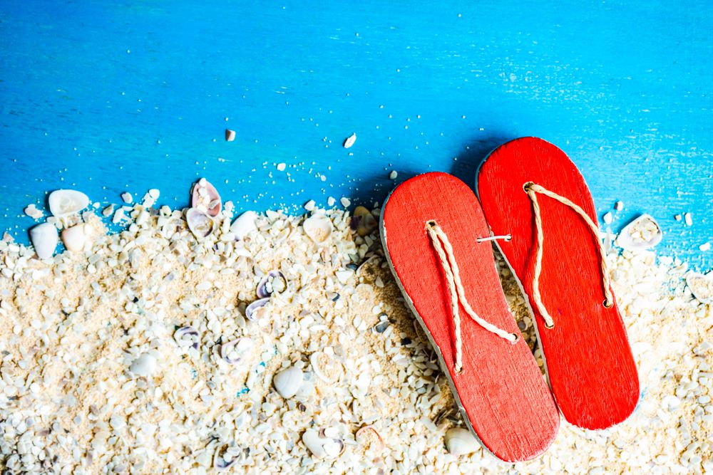 Flat lay of flip flips and sand on blue background