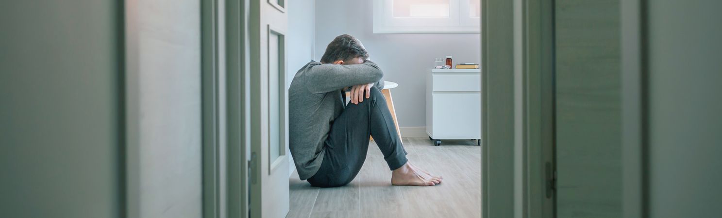 Man with mental disorder crying sitting on room floor