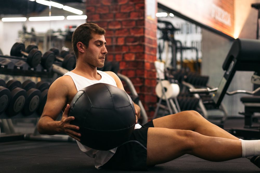 young man doing weight ball abs exercise in a gym