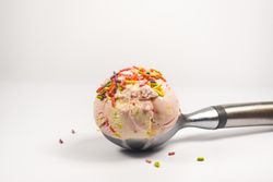 Side view of pink ice cream scoop with sprinkles on table