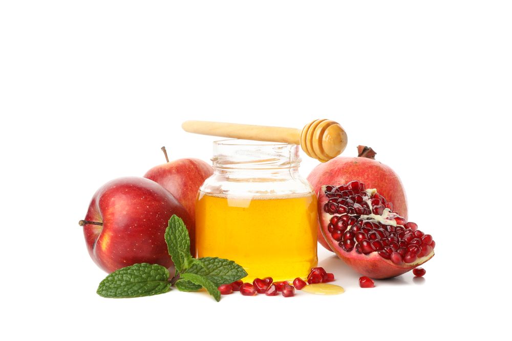 Pot of honey with dipper, open pomegranate and apples