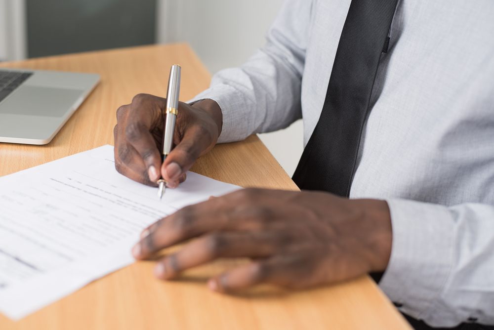 Man in gray suit jacket writing on paper