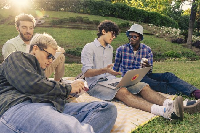Diverse group of young students working and relaxing together outdoors in a park.