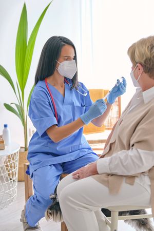 Physician with syringe and vaccine against crop patient at home