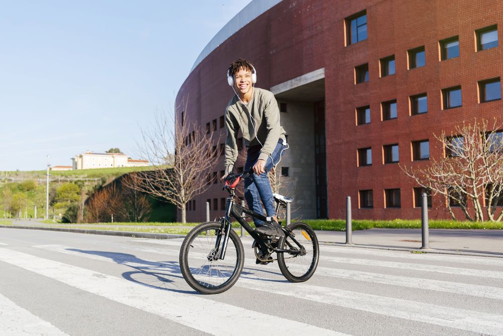 Young happy Black man in headphones riding bicycle