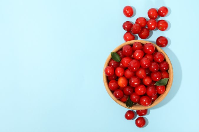 Bowl with fresh red cherry on blue background, top view