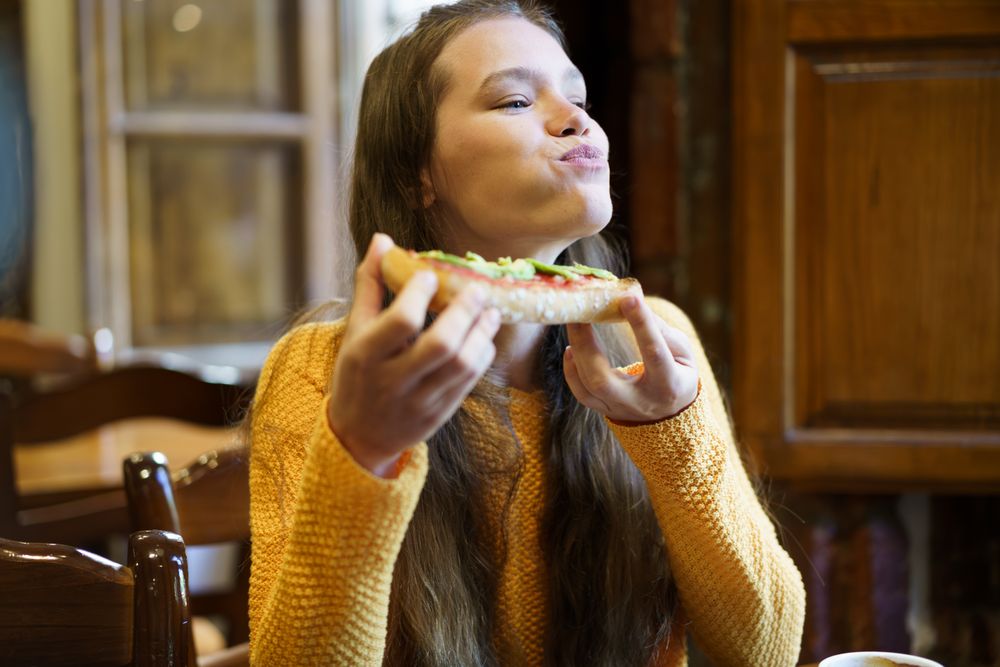 A Joyful Young Woman Delightedly Enjoying a Slice of Pizza in a Cozy Restaurant Atmosphere