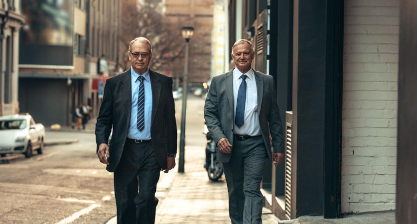 Two mature business people walking down sidewalk