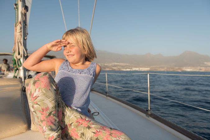 Smiling girl sitting on edge of yacht on water