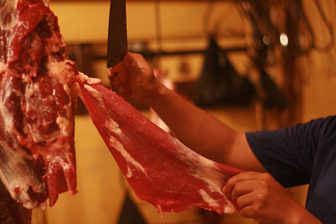 Man with knife cutting a slice of raw meat