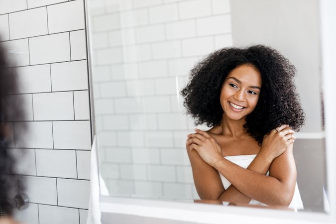 Black woman smiling at herself in the mirror with her arms around her
