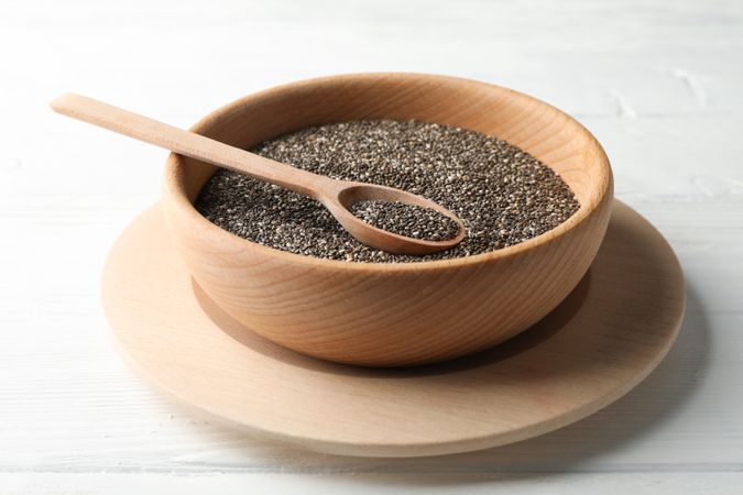 Wooden bowl with chia and spoon on wooden background, close up