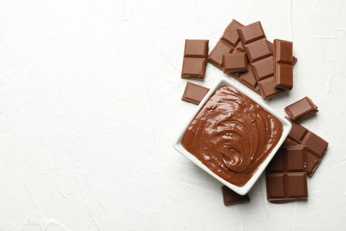 Bowl with chocolate and chocolate pieces on neutral background