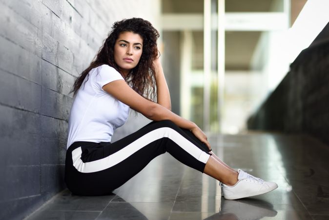 Thoughtful female in leggings sitting outside of building entrance