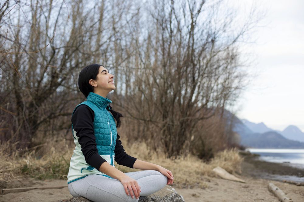 Happy young female with her eyes closed sitting on a log meditating